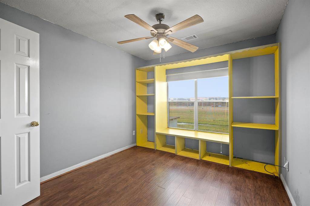 This room features a large window with a built-in yellow shelving unit, providing ample natural light and storage. It has a ceiling fan and wood flooring, offering a bright and functional space.  Not pictured is a large walk-in closet, consistent in all four bedrooms.