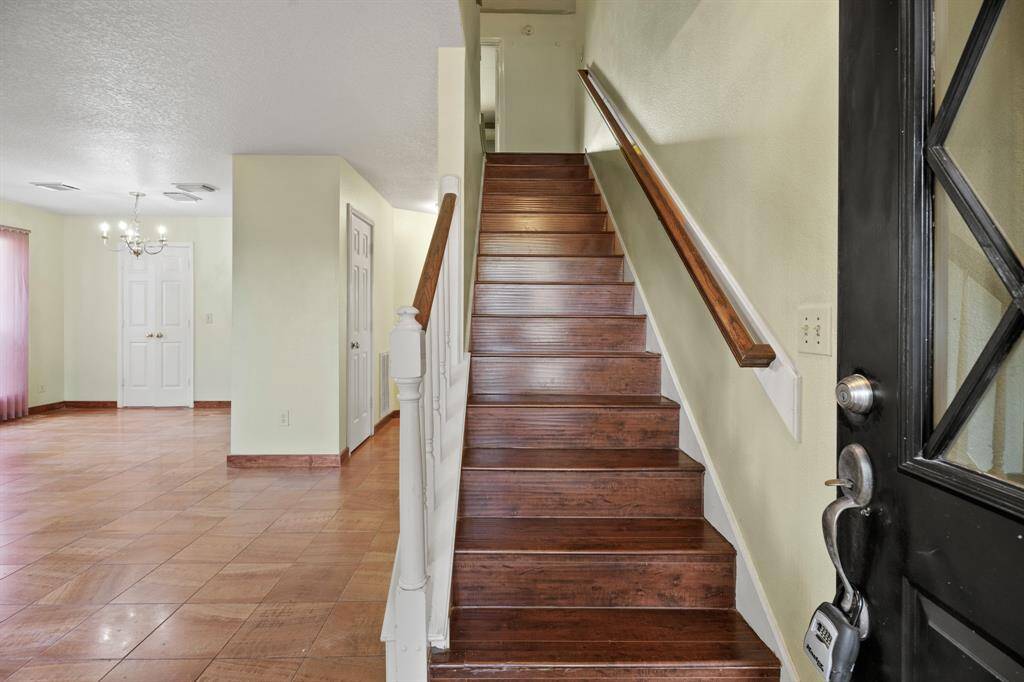 A welcoming entryway with a luxury vinyl wooden staircase leading to the upper floor. The space features tiled flooring, light walls, and a chandelier, providing a bright, open feel.