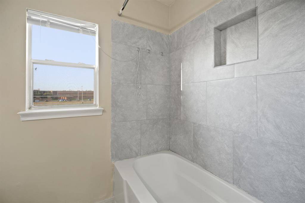 This bathroom features a tub with sleek gray tile surround, a built-in niche for storage, and a window for natural light.
