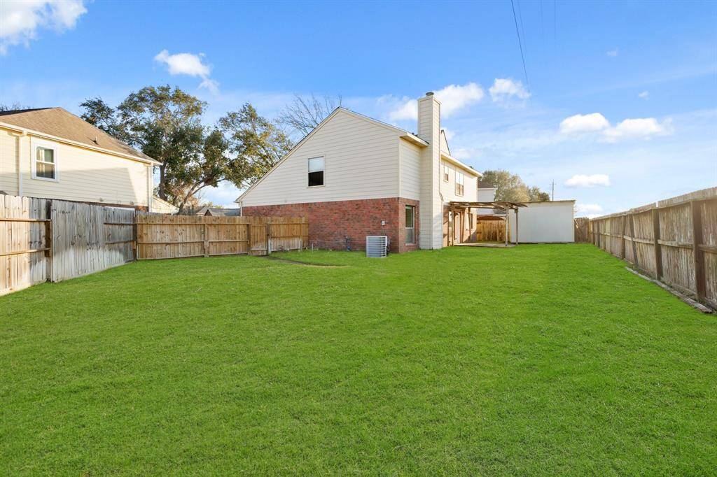 Spacious backyard with lush green lawn, surrounded by a wooden fence for privacy. The house features a brick and siding exterior, a covered patio, and a large open area, ideal for outdoor activities or gardening.