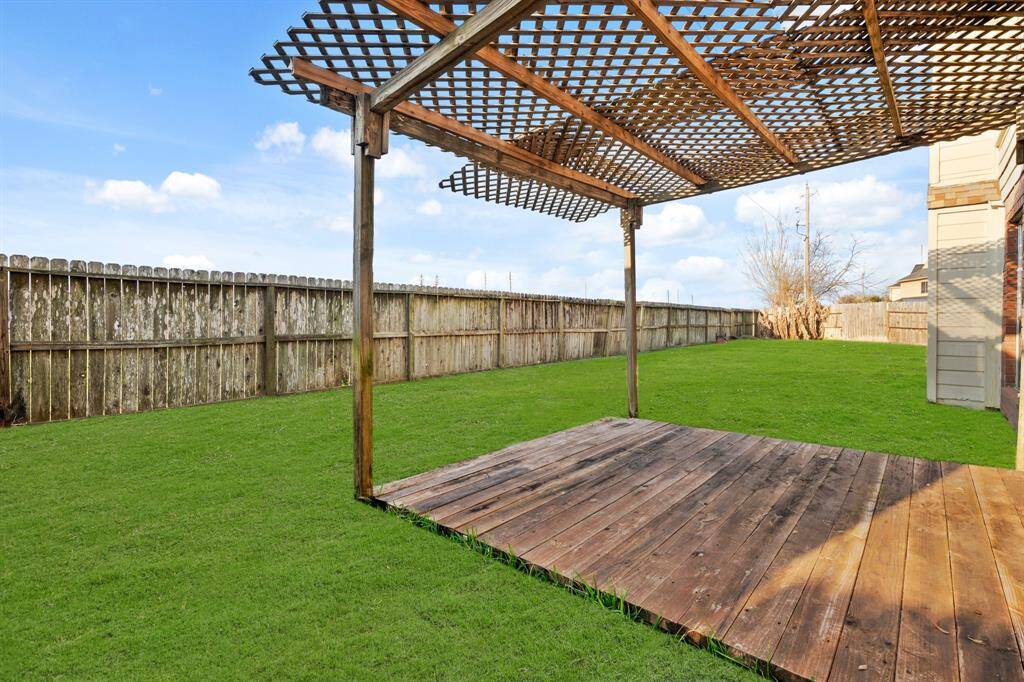 This photo showcases a spacious backyard with a well-maintained lawn, featuring a wooden deck and a pergola for outdoor relaxation. The area is enclosed by a wooden fence, providing privacy and a serene setting.