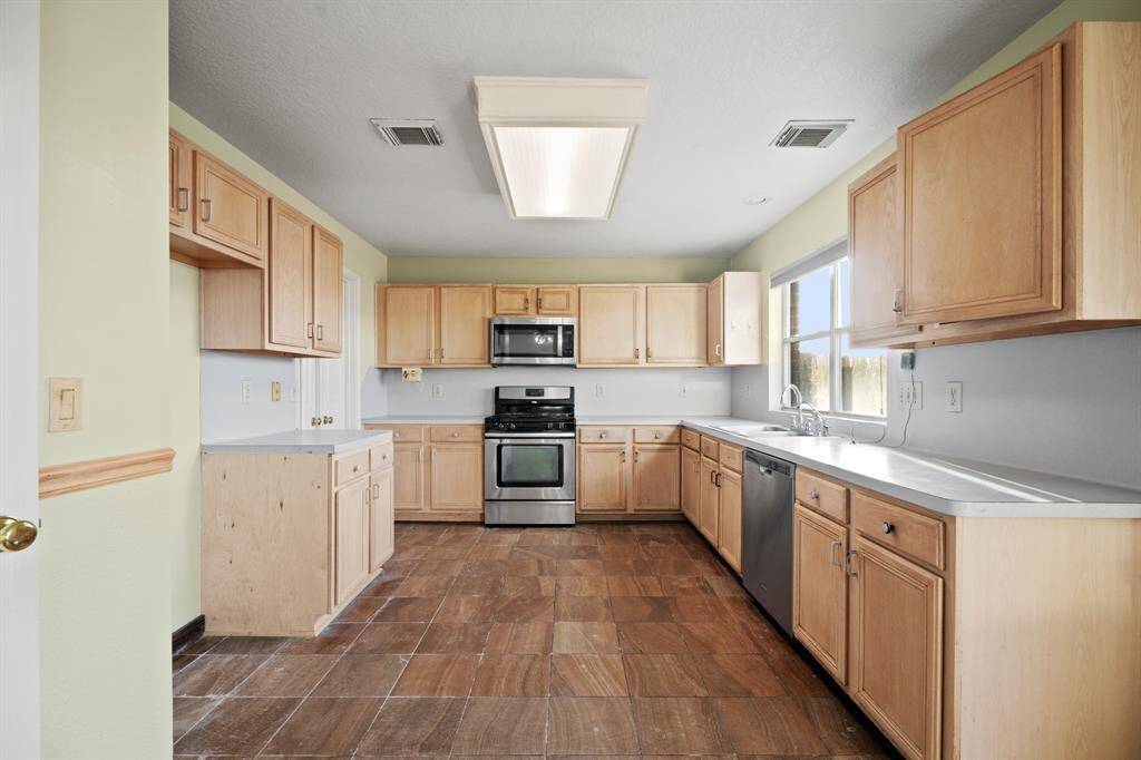 This spacious kitchen features natural wood cabinetry, stainless steel appliances, and ample counter space. The large window provides plenty of natural light, and the tiled floor adds warmth to the room. Perfect for cooking and entertaining.