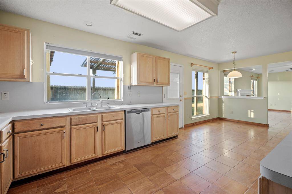 This bright kitchen features ample natural light, wooden cabinets, a dishwasher, and spacious countertops. The open layout flows into the breakfast nook and family room areas, creating an inviting space for meals and gatherings.