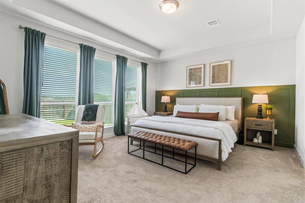 The owner's suite located on the first floor, offering tiered ceiling, carpet for comfort, large windows for abundant natural light.