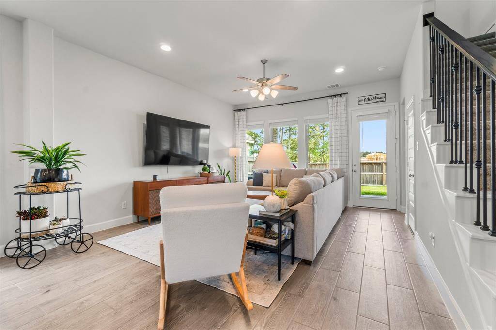 Living room features recessed lighting, ceiling fan, and. wood-style tile flooring. Access to the outdoors to the coverd patio. A wrought iron railing along the staircase leading upstairs.