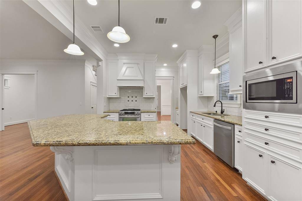 Inviting chef's kitchen is open to the family room and features a spacious layout with elegant granite countertops, modern stainless steel appliances, and ample white cabinetry. The island offers additional prep space and seating, complemented by stylish pendant lighting and warm wood floors.