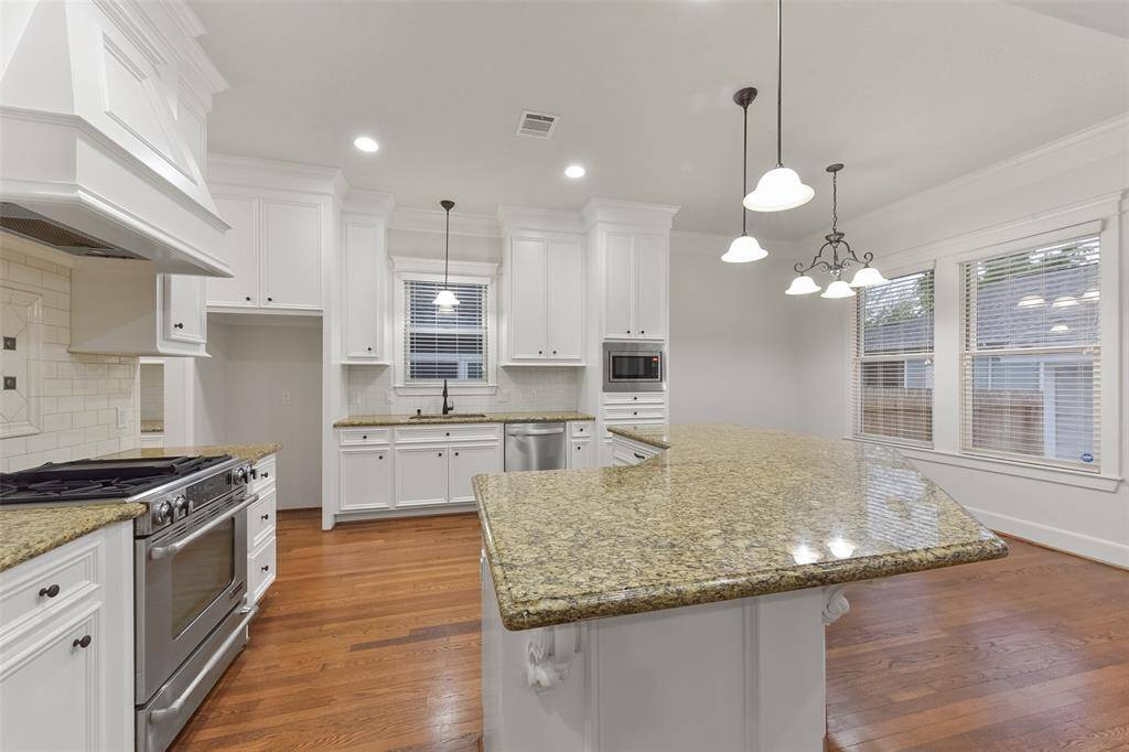 Another view of the kitchen featuring granite countertops, white cabinetry, and stainless steel appliances, including a large freestanding stove. The open layout is enhanced by warm hardwood floors and ample natural light from the large windows. Modern pendant lighting adds a stylish touch.