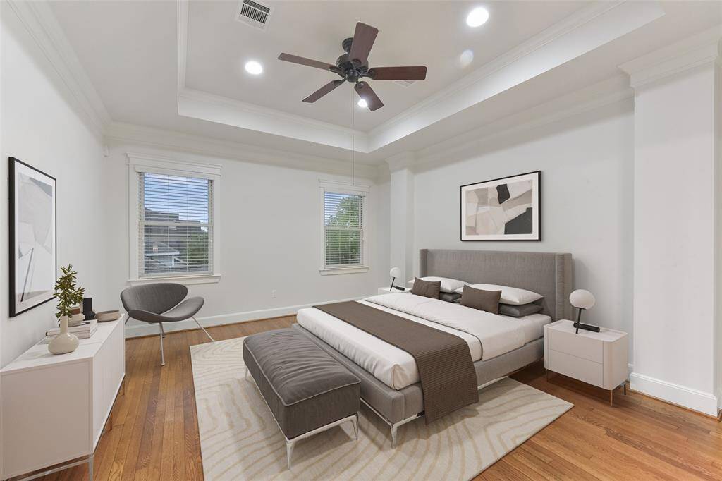 This spacious, light-filled Primary suite features hardwood floors, a tray ceiling with recessed lighting, and a ceiling fan. Two large windows with blinds, providing natural light and a fresh, airy feel. Virtually staged.