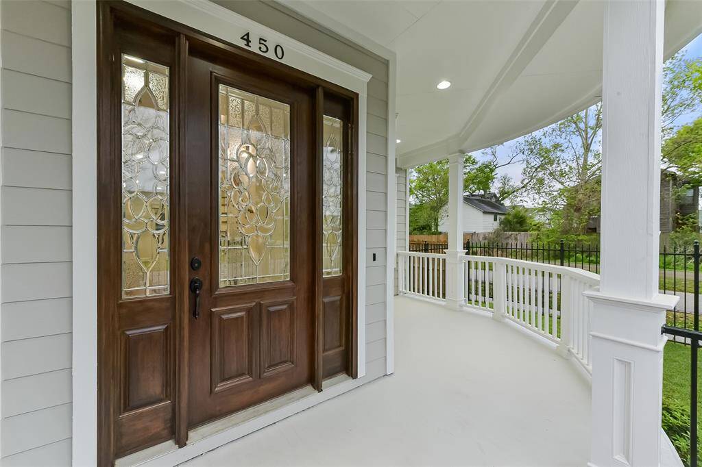Welcome home through this richly crafted wooden door featuring decorative glass panels. Covered front porch with white railings enhances the home’s inviting entrance.
