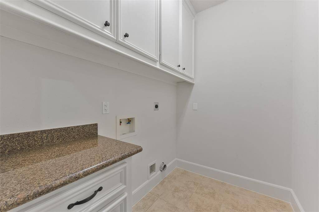This spacious laundry room with white cabinetry and a sleek granite countertop is equipped with utility hookups for a washer and dryer.