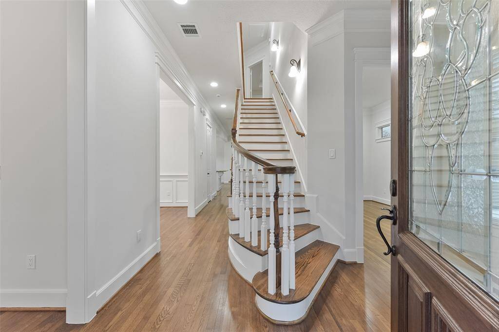This bright and elegant entryway with a curved wooden staircase, hardwood floors, and a decorative glass front door provides a welcoming ambiance.