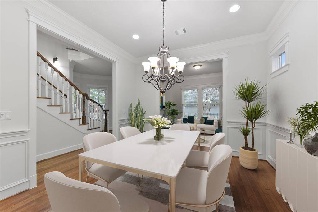 Light-filled and bright elegant formal dining room with hardwood floors, white wainscoting, and a classic chandelier. Formal dining room is open to the formal living and to a staircase with wooden railings featuring large windows offering plenty of natural light. Virtually staged.
