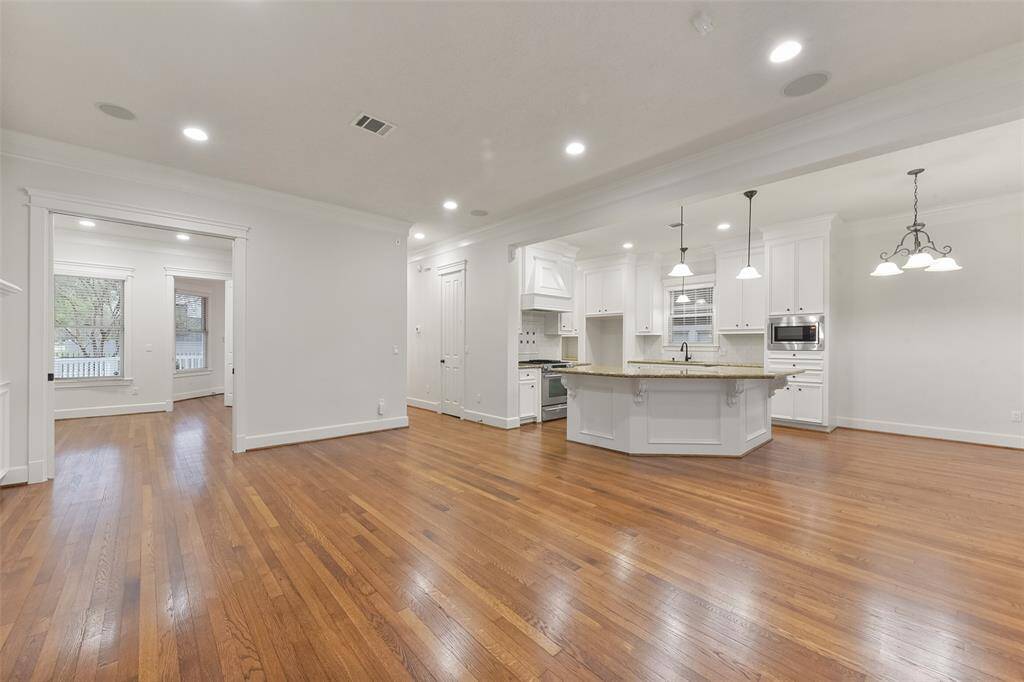 Another view of the spacious, open-concept living area with hardwood floors and recessed lighting open to the modern kitchen featuring a large island, breakfast bar, white cabinetry, and stainless steel appliances, creating a bright and inviting atmosphere.