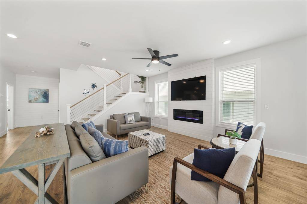 Living room features beautiful flooring, aceiling fan, high ceilings, and windows.