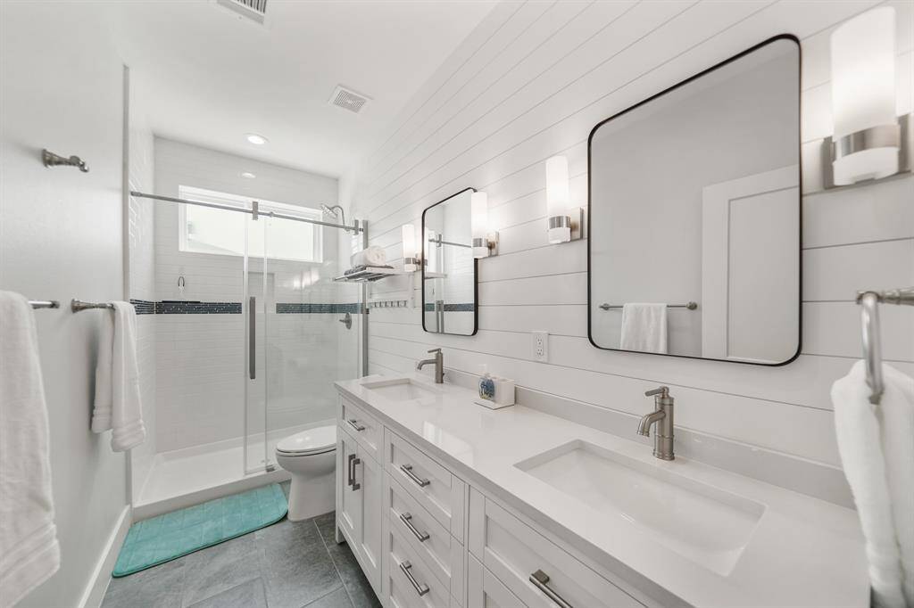 Primary bathroom features dual sinks, white cabinets, tile floors, and a walk-in shower with tile surround.