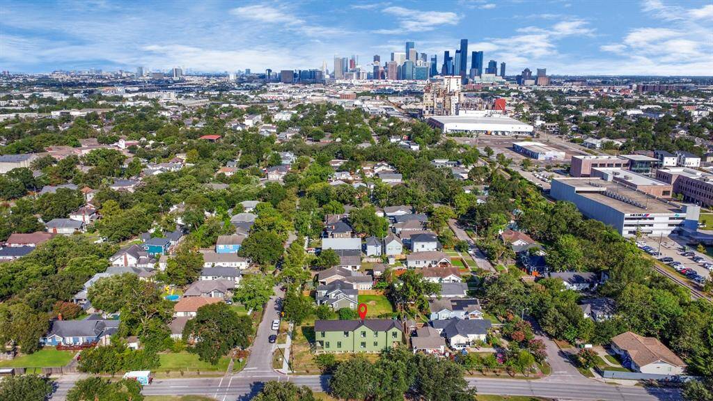 This aerial photo showcases a residential area with a mix of single-family homes, lush greenery, and spacious yards, marked by a red location pin. The neighborhood enjoys proximity to a vibrant city skyline, offering a blend of suburban tranquility and urban convenience.