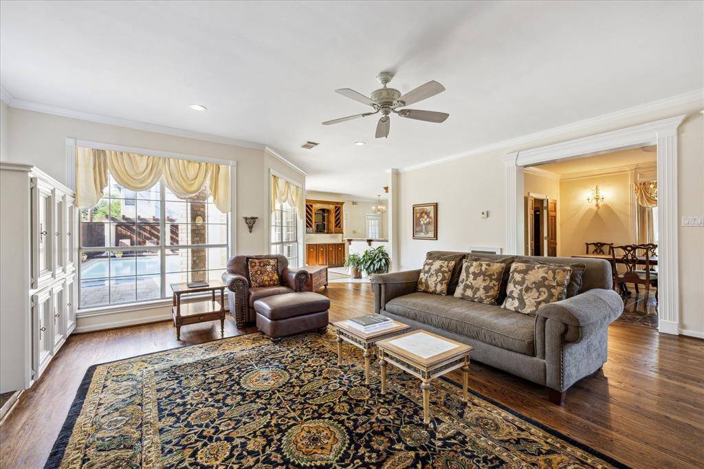 This family room connects seamlessly to the dining area and bar, featuring wood floors, crown molding, and large windows with views of the pool.