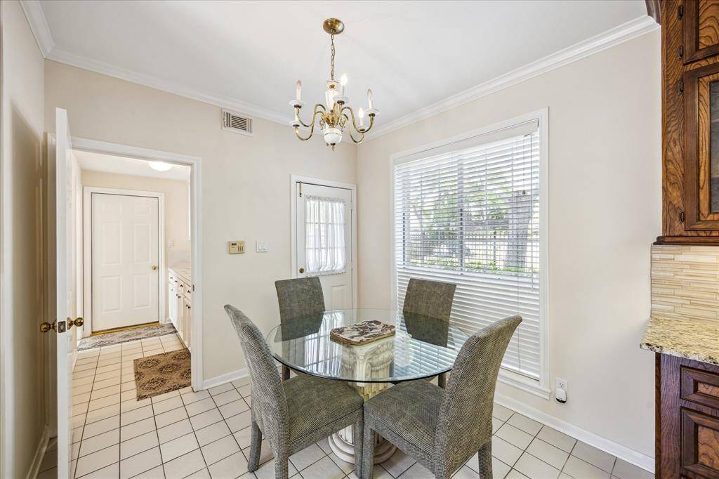 This bright breakfast room features tile flooring, crown molding, and a large window that overlooks the side yard.