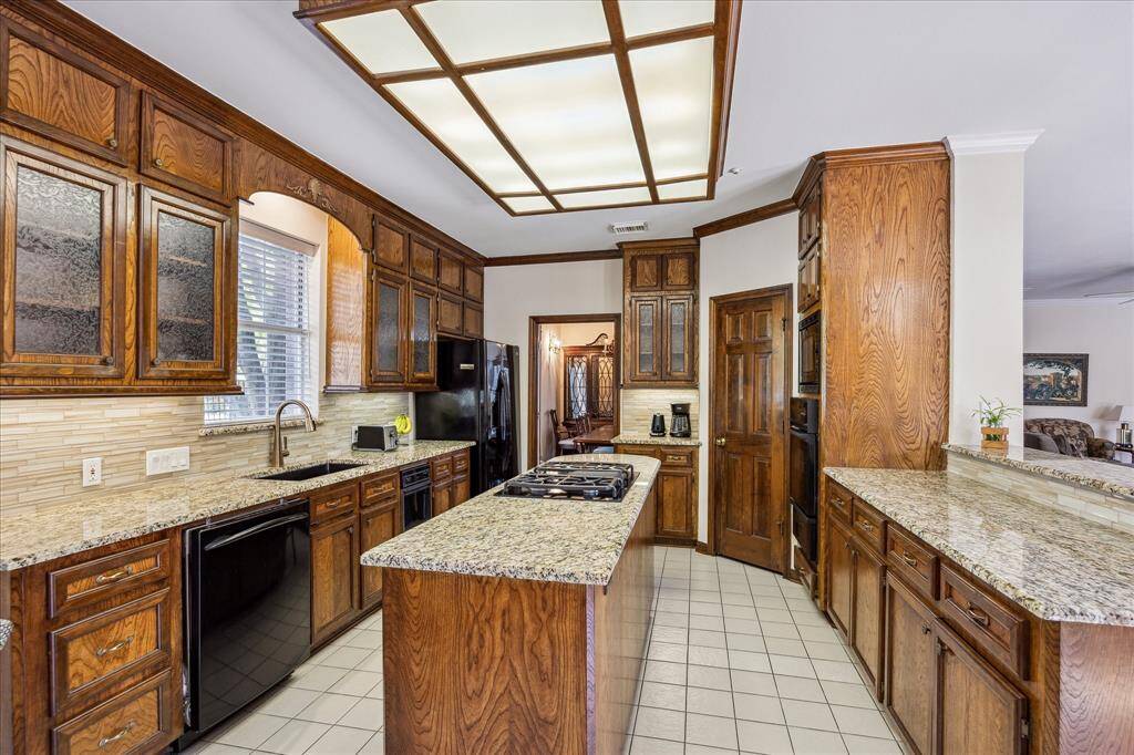This kitchen offers extensive granite counter space, a large center island with gas cooktop, and generous cabinetry for storage.