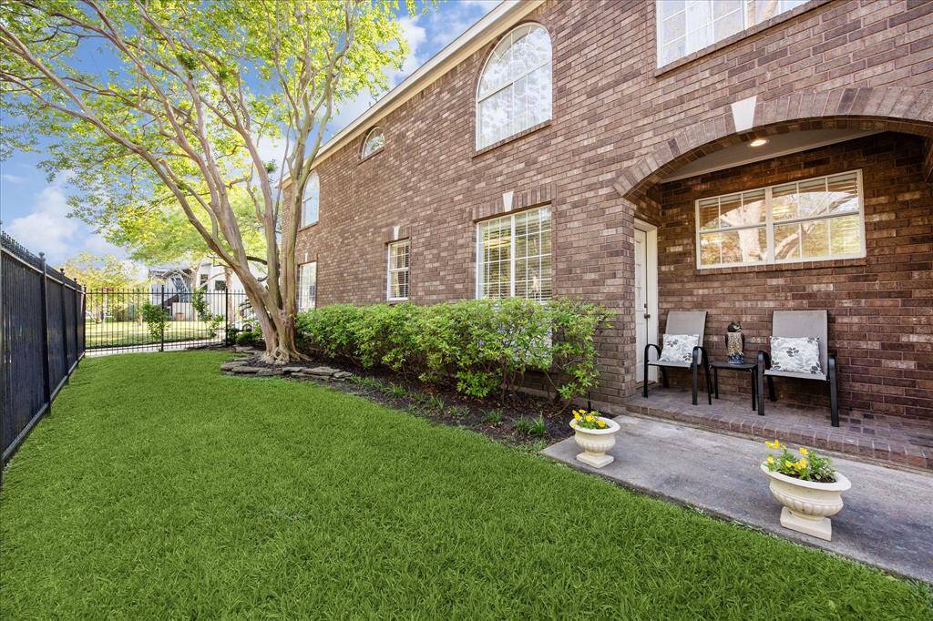 This gated side yard offers a private green space with mature trees, manicured hedges, and a cozy covered patio—perfect for quiet outdoor lounging or casual conversation.