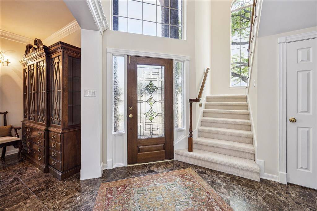 This entryway features soaring ceilings, large windows that fill the space with natural light, and a graceful staircase that curves toward the upper level.