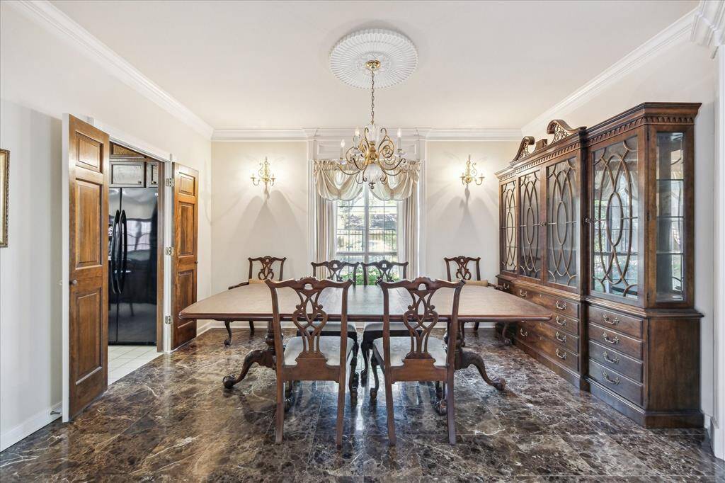 This formal dining room features stone flooring, crown molding, and a large window that brings in natural light.