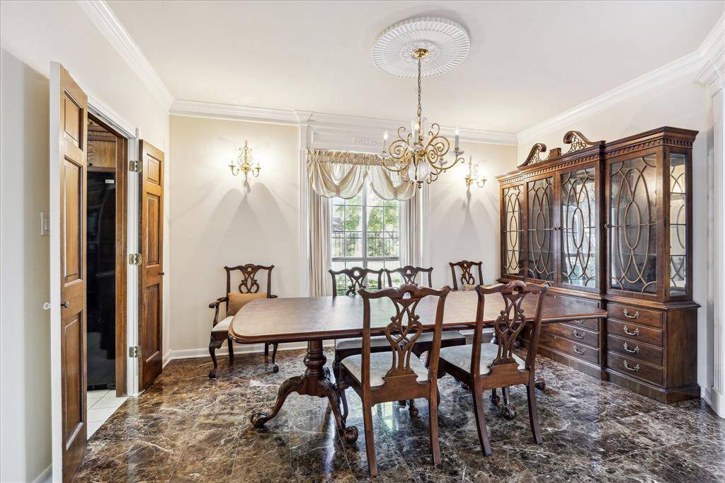 This elegant dining room features marble floors, detailed crown molding, and a large window that fills the space with natural light.