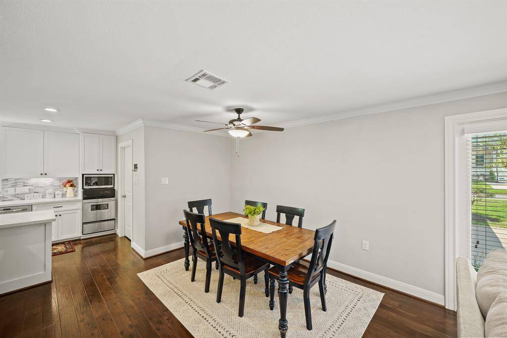 The Dining Area is Open to the Kitchen and the Living Area/Den and features Walnut Hued Handscraped Hardwood Floors, Crown Molding, Extended Baseboards, and Light Grey Designer Paint with White Trim.