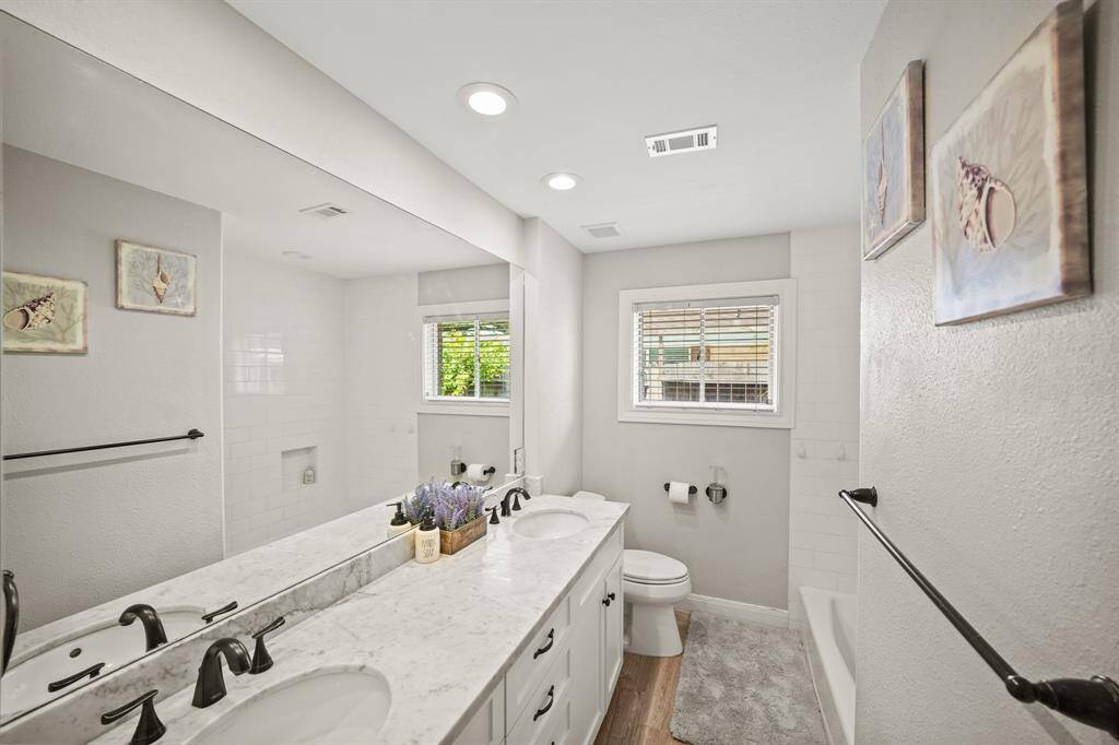 The Hall Bath/Guest Bath features White Shaker Style Cabinets and Deep Drawers, Dual Undermount Sinks, Oil Rubbed Bronze Faucets, LED Recessed Lighting, Wall Mounted Mirror, Oil Rubbed Bronze Hardware, Kohler Full Tub/Shower with White Subway Tile Surround,  Kohler Commode, Oil Rubbed Bronze Accessories (Towel Rack, etc.), Light Grey Designer Paint with White Trim, Grey Hued Wood Plank Porcelain Tile Floors, and Extended Baseboards.