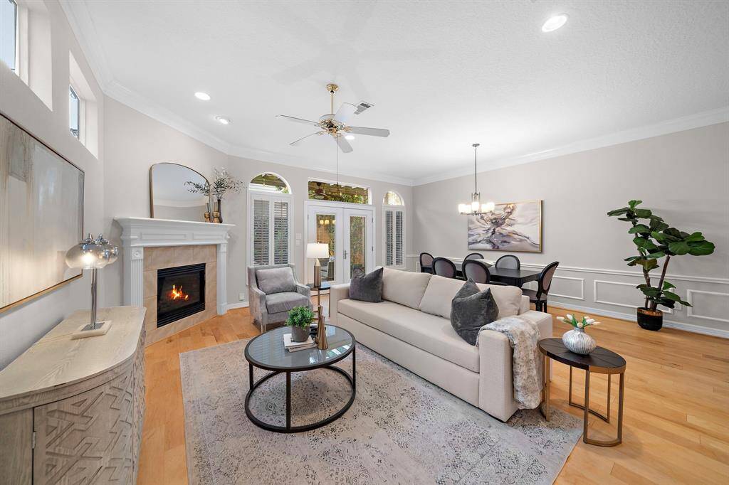 Natural light dances through transom windows and French doors in this inviting living space, anchored by warm hardwood floors and a cozy gas fireplace. Elegant millwork and soft neutral tones complement the open layout, offering easy flow to the dining area and backyard retreat.