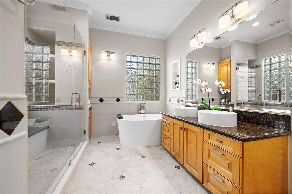 A spa-like retreat, the ensuite bath features a deep soaking tub, dual vessel sinks, granite countertops, and custom cabinetry beneath a wall-wide mirror.
