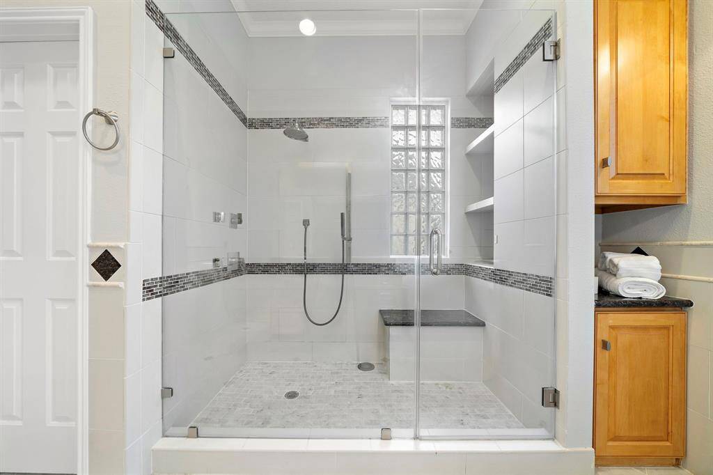 Step into the oversized frameless glass shower with dual shower heads, built-in bench seating, and sleek tile accents for a daily touch of luxury.