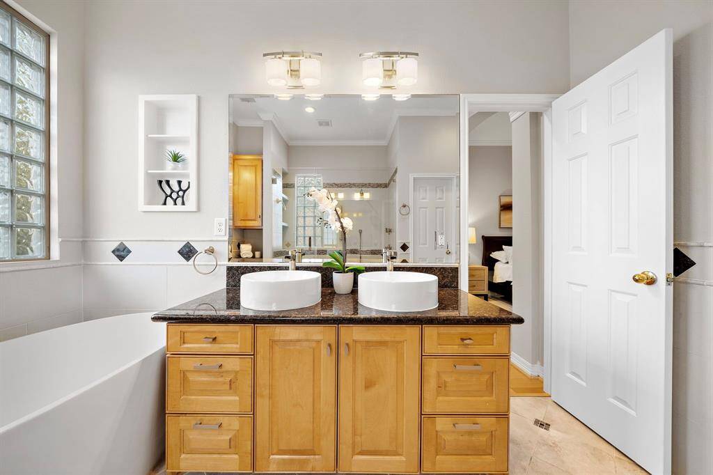 Dual vessel sinks and granite countertops provide a luxe touch, while abundant cabinetry ensures effortless organization. Relax in the deep soaking tub or enjoy the expansive glass-enclosed shower, all framed by fresh finishes and natural light streaming through glass block windows.