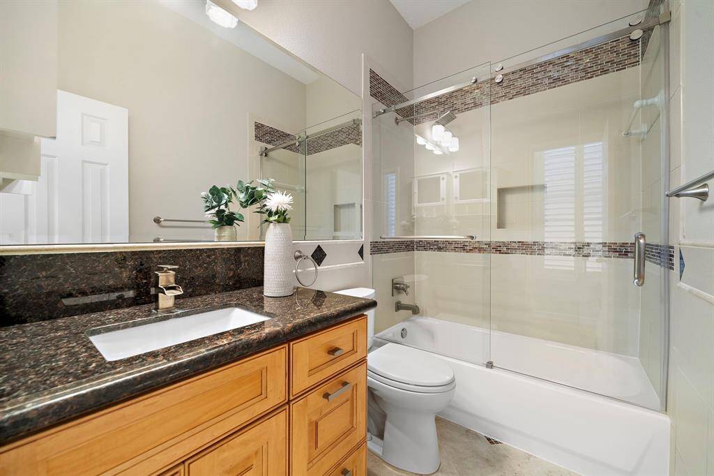 The secondary bath features sleek granite counters, updated fixtures, and a tub-shower combo with glass enclosure and stylish tile inlay.