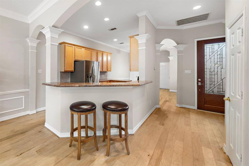 The kitchen blends charm and function with granite countertops, maple cabinetry, and a raised breakfast bar perfect for casual mornings. Arched entryways and a rich wood door elevate the warm, welcoming aesthetic of the first-floor layout.