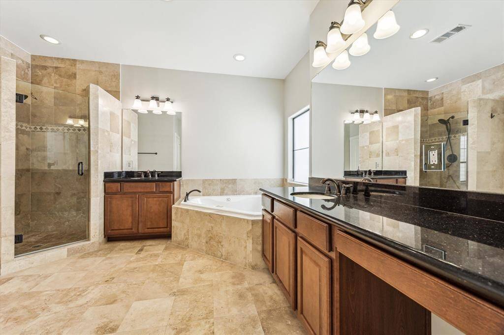 En-site bathroom features a glass shower, tub, & travertine tile.