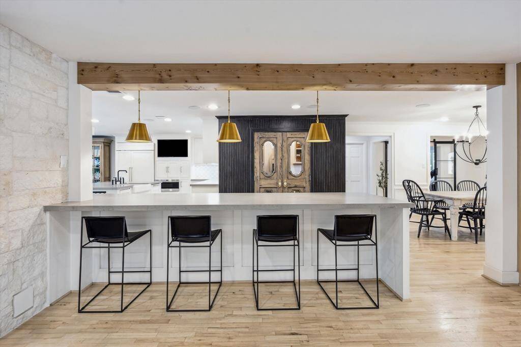 This modern kitchen features a large penisula with seating for four, accented by stylish gold pendant lights. It opens into a dining area with elegant black chairs, creating a welcoming and functional space for entertaining.