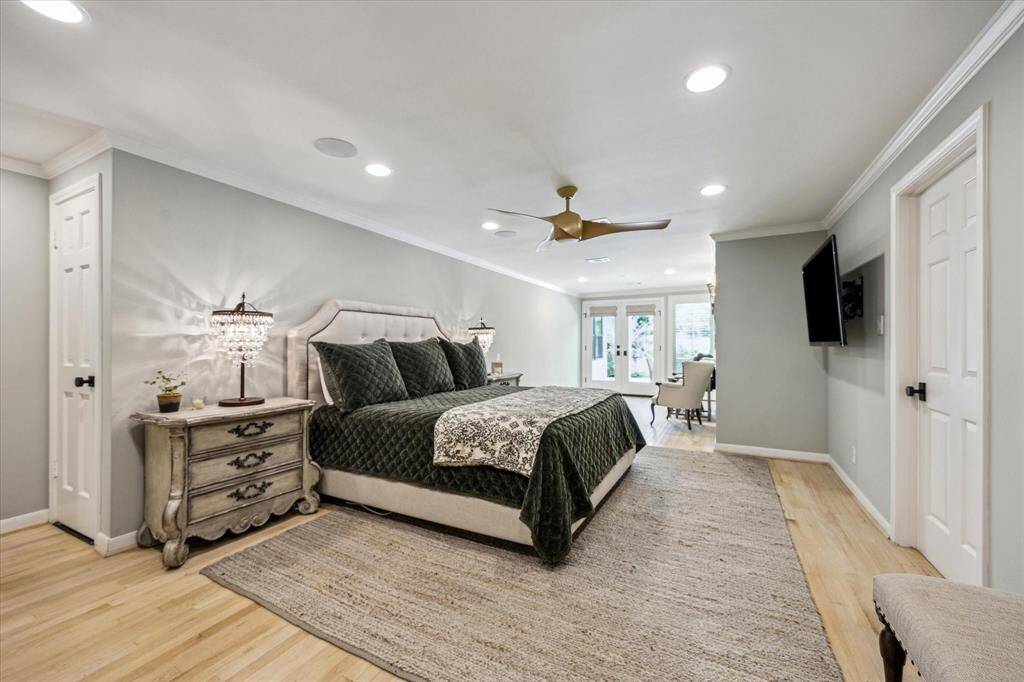 This spacious primary bedroom features a sitting area.  The room is well-lit with recessed lighting and has light wood floors. French doors lead to an outdoor area, providing plenty of natural light.