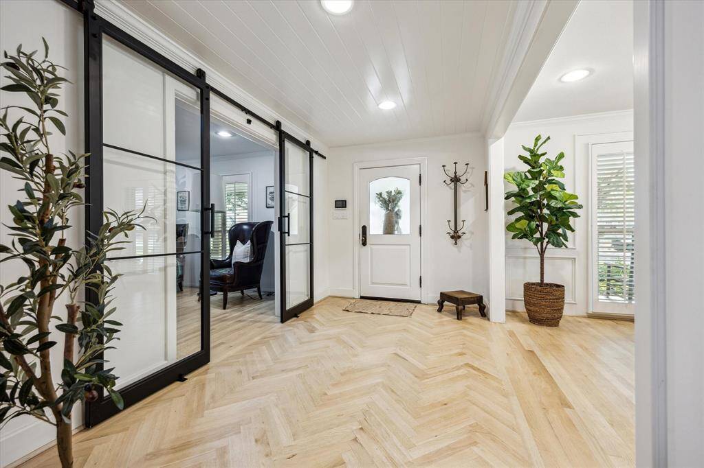 Bright and welcoming entryway with stylish herringbone wood flooring, modern glass sliding doors that lead to a study, and abundant natural light.