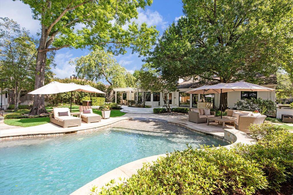 This inviting outdoor space features a sparkling pool surrounded by lush greenery and mature trees. Comfortable lounge chairs and shaded seating areas provide perfect spots for relaxation and entertaining. The well-maintained garden and patio create a serene and private retreat.