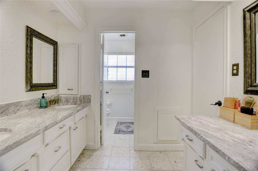 View of the vanity area of the secondary bathroom with double sinks and an additional counter. The tub/toilet area also features linen storage behind the door.