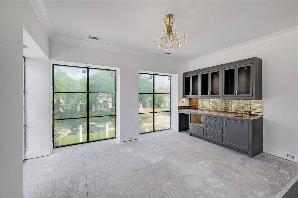 The primary suite also includes a retreat area with built-in cabinets, sink, plus space for a mini fridge and microwave. Large windows overlook the front yard. Stage of construction as of April 17, 2025.