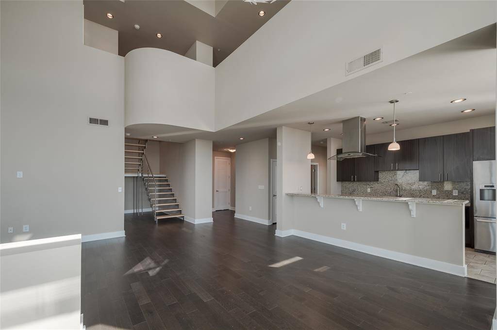 The open-concept layout features a chef-inspired kitchen with sleek cabinetry, quartz countertops, and high-end stainless steel appliances. The lofted second level offers the perfect flex space—ideal for a home office, creative studio, or secondary living area—overlooking the dramatic main living space below.