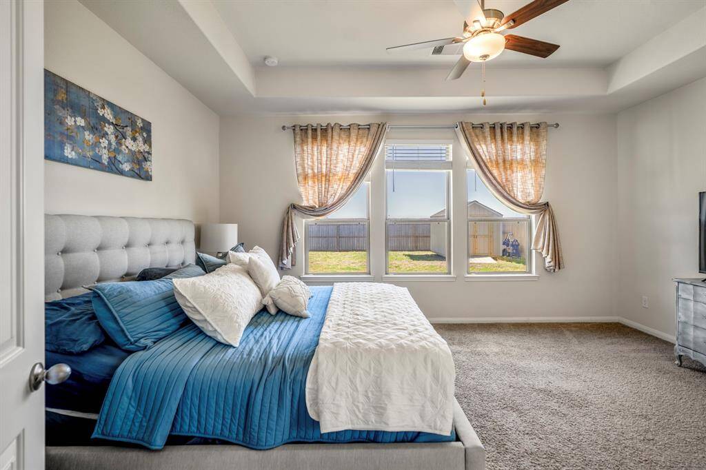Spacious primary bedroom with large windows and an elegant recessed ceiling.