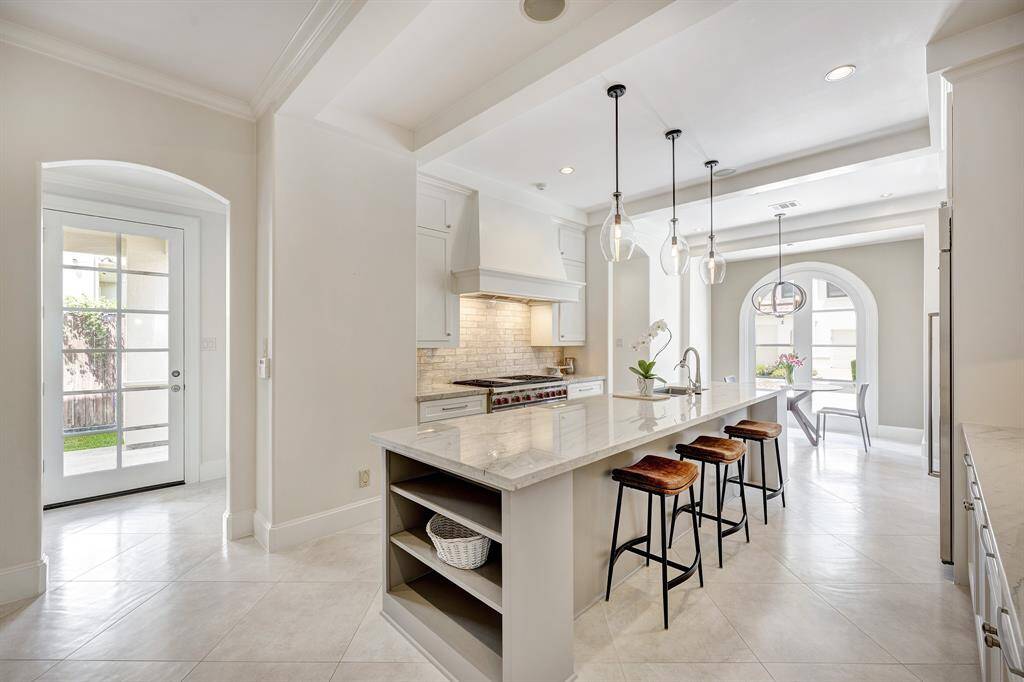 Anchored with ethereal Italian tile, quartzite countertops and high-end appliances, this kitchen is absolutely dreamy! To the left in this photo you can see the door to the porte-cochere with the mudroom and utility room flanking either side