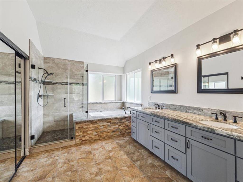 NEWLY RENOVATED PRIMARY BATHROOM WITH A WALK-IN SHOWER, SOAKING TUB WITH STONE SURROUND, DUAL SINK VANITY WITH NEW CABINETRY, AND GRANITE COUNTERTOPS.