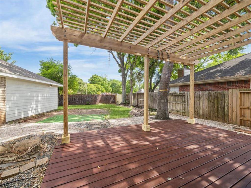 RELAX OR ENTERTAIN ON THE ELEVATED WOOD DECK WITH A PERGOLA, SURROUNDED BY MATURE TREES AND PRIVACY FENCING.