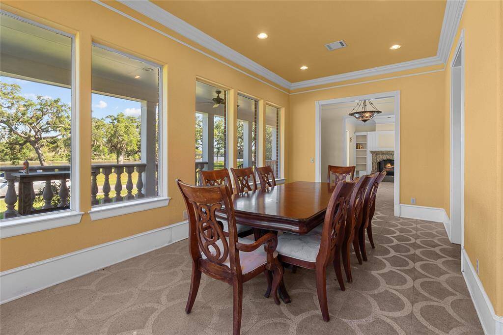 Bright dining area with large windows offering scenic views. Features warm yellow walls, patterned carpet, and elegant wooden furniture. Connected to the kitchen, creating a convenient and inviting space for meals and gatherings.