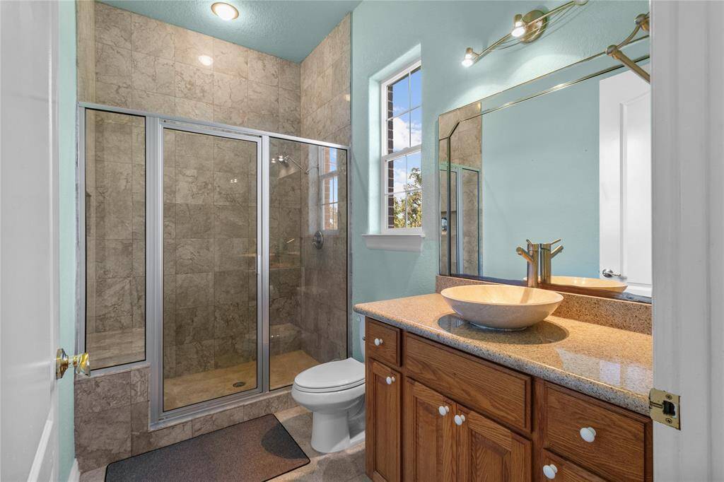 This inviting downstairs bathroom features a sleek glass shower, elegant vessel sink, and a convenient built-in vanity, all complemented by warm wood cabinetry.