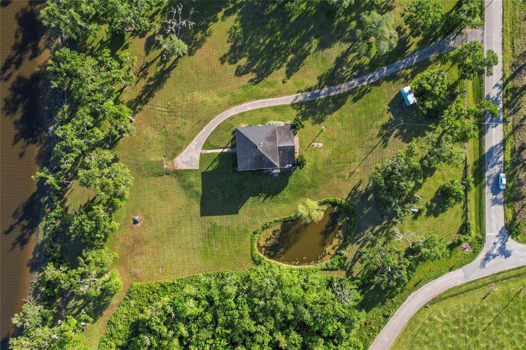 Expansive property with lush greenery, a charming pond, and a scenic driveway leading to a beautifully positioned home, offering tranquility and privacy.